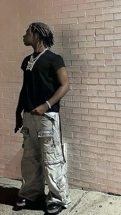 a man with dreadlocks standing in front of a brick wall wearing cargo pants