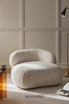 a white chair sitting on top of a wooden floor next to a table and lamp