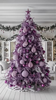 a purple christmas tree with ornaments and lights on the top, in a white room