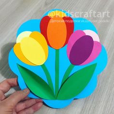 a person holding up a paper flower on top of a table