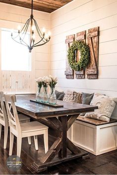 a dining room table and bench with two wreaths on the wall