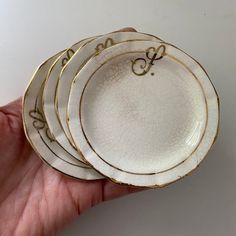 a hand holding four white and gold plates