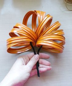 a hand is holding an orange piece of art that looks like a spirally leaf