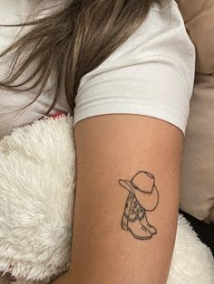 a woman with a hat and boots tattoo on her arm, sitting next to a teddy bear