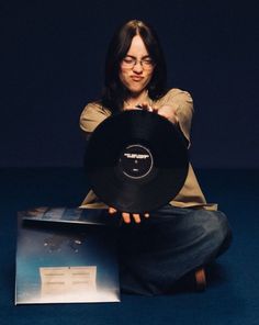 a woman sitting on the floor holding up a record