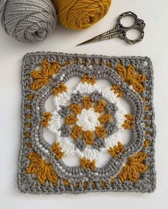 a crocheted square with two balls of yarn next to it and a pair of scissors