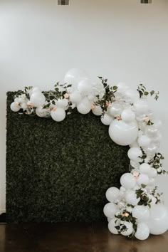 white balloons and greenery are arranged in the shape of an arch