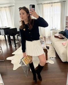 a woman is taking a selfie in her living room wearing a white pleated skirt and black cardigan