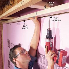 a man holding a drill and screwdriver in front of a wall with pink walls