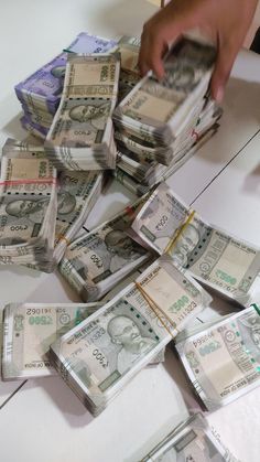 a pile of twenty dollar bills sitting on top of a white table next to a person's hand