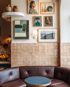 a brown leather couch sitting in front of a wall with pictures on the wall above it