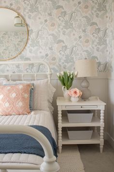 a white bed sitting in a bedroom next to a nightstand with flowers on top of it