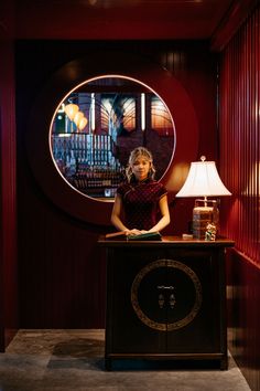 a woman sitting at a desk in front of a round window with a clock on it