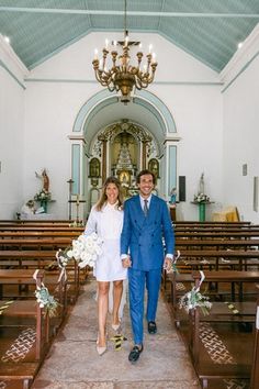 a bride and groom walking down the aisle of a church with chandeliers hanging from the ceiling