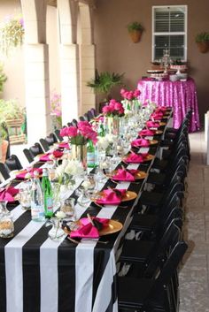 a long table is set with black and white striped tables cloths, pink napkins, and wine bottles