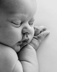 a black and white photo of a baby with its head resting on the arm of his mother