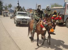 two soldiers riding on the back of a brown horse down a street next to cars