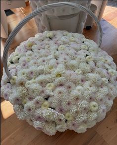 a basket filled with white and pink flowers on top of a wooden floor next to a table