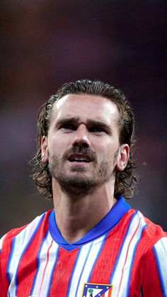 a man with long hair wearing a red and blue striped shirt looking up at the sky