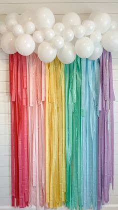 balloons and streamers are hanging from the ceiling in front of a rainbow - colored wall