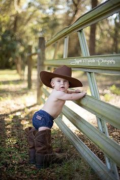 a little boy wearing a cowboy hat leaning against a fence