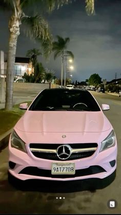 a pink car is parked on the side of the road at night with palm trees in the background