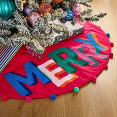 a christmas tree with presents under it on the floor next to a red merry mat