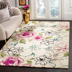 a white rug with pink and green flowers on it in front of a beige couch