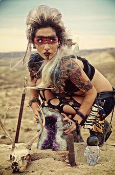 a woman with long hair and tattoos kneeling next to an animal skull holding a knife