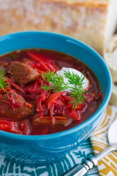 a blue bowl filled with meat and red cabbage soup next to bread on a table