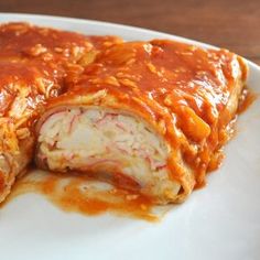 a white plate topped with meat and sauce covered enchilada roll on top of a wooden table