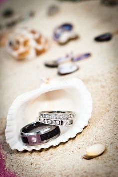 two wedding rings sitting in an oyster shell on the beach with seashells around them