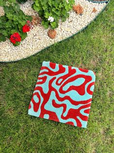 a red and blue rug sitting on top of a green grass covered field next to flowers