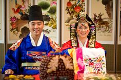 two people dressed in traditional chinese clothing standing next to each other with food on the table