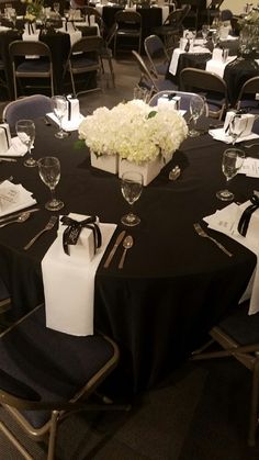 a black table with white flowers and napkins on it is set up for an event