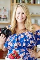 a woman holding a camera in front of a cake with strawberries on the bottom