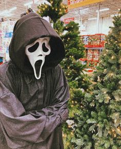 a person in a ghost costume standing next to a christmas tree