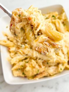 a white plate topped with pasta covered in chicken and cheese sauce next to a fork