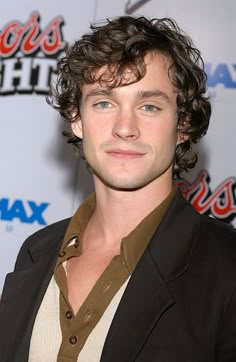 a young man with curly hair wearing a brown shirt and blazer at an event