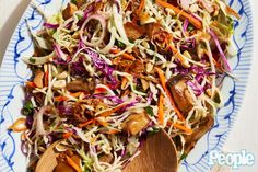 a salad with carrots, cabbage and nuts on a blue and white plate next to a wooden spoon