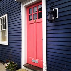 a blue house with a red door and white trim on the outside wall, along with a planter filled with flowers