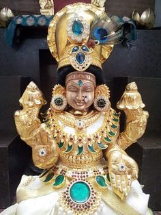 the statue is gold and white with green jewels on it's head, sitting in front of a black background