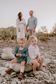 two toddlers sitting on rocks with their parents in the background