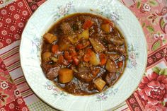 a white bowl filled with stew on top of a red and green table cloth next to a spoon