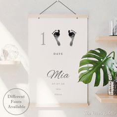 a white poster hanging on a wall next to a potted plant and two baby feet