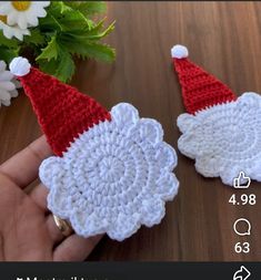 two crocheted santa hats on top of each other next to a bouquet of flowers