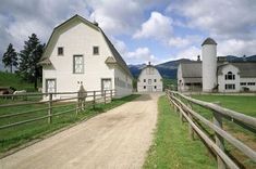 a farm with two white barns and a dirt road leading to the barnyards