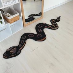 a black and brown snake rug on the floor next to a white book shelf with a mirror