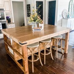 a kitchen island made out of wood with stools around it and flowers in vase on top