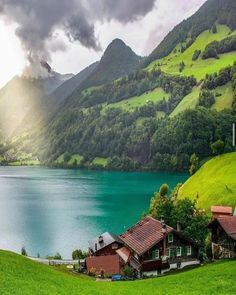 a lake surrounded by lush green mountains under a cloudy sky with sun shining through the clouds